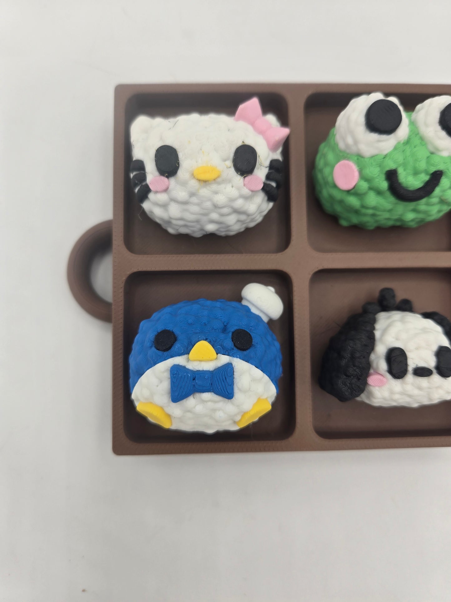 Close-up of the white kitty and blue penguin rice ball clickers in the Sanrio themed tray fidget — textured 3D printed rice detail
