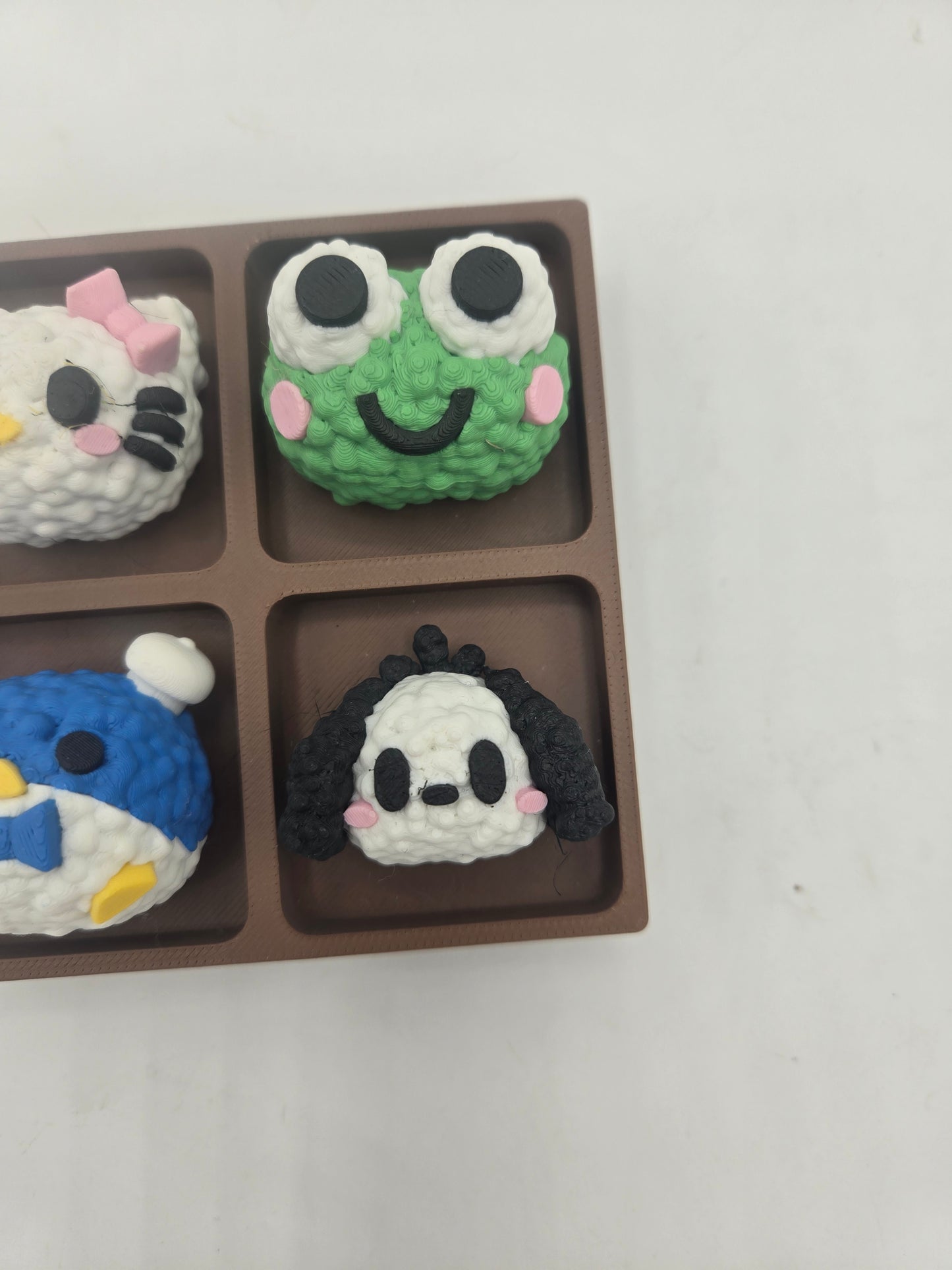 Close-up of the green frog and floppy-eared puppy rice ball clickers in the Sanrio themed tray fidget — textured 3D printed rice detail