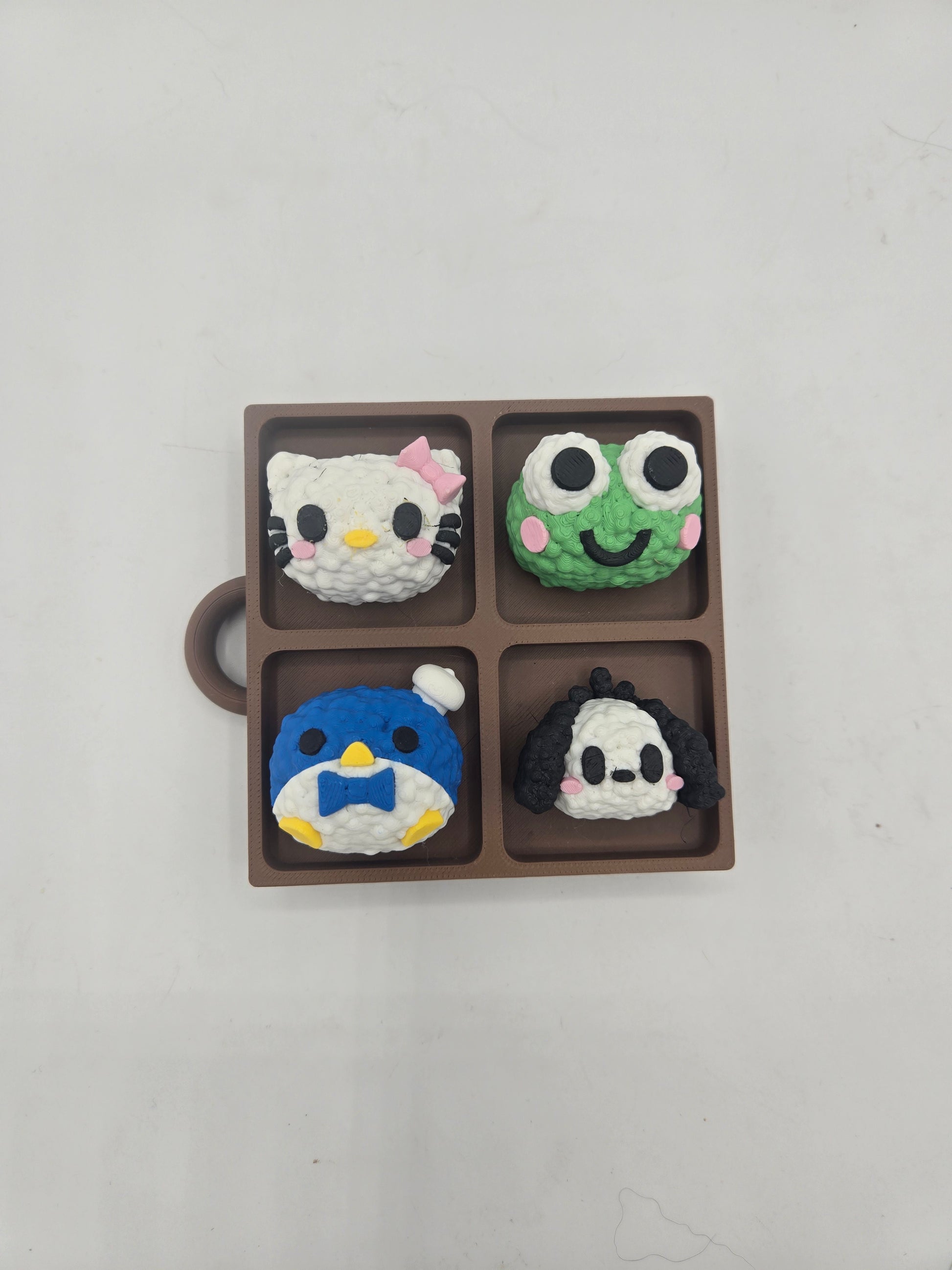 Overhead view of the Sanrio themed rice ball tray clicker board — four kawaii rice ball characters in a four-section bento-style tray, 3D printed