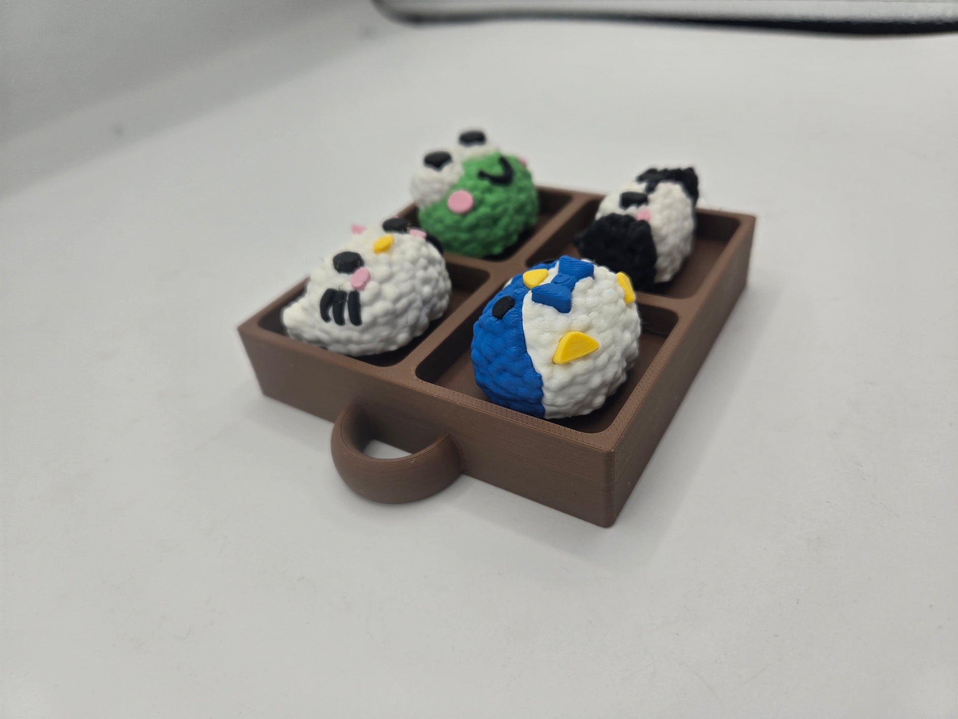 Angled view of the Sanrio themed rice ball tray clicker fidget showing the tray depth and keychain loop, four rice ball characters, 3D printed