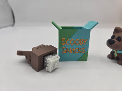 Scooby Snacks key clicker 3D print tipped over to show the mechanical keyboard switch inside the base, with box and dog figurine