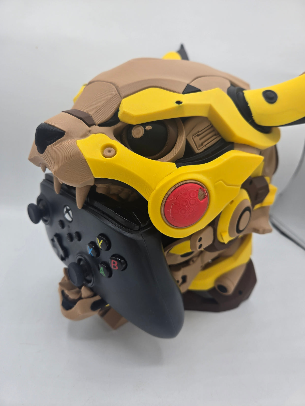 Mekachu Mecha Monster controller holder 3D print front three-quarter view holding a black Xbox controller in its open jaw, yellow armor plating and red cheek