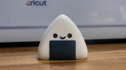 Kawaii onigiri figure front view — 3D printed white rice ball with a smiling face and dark seaweed band, standing on a wooden desk
