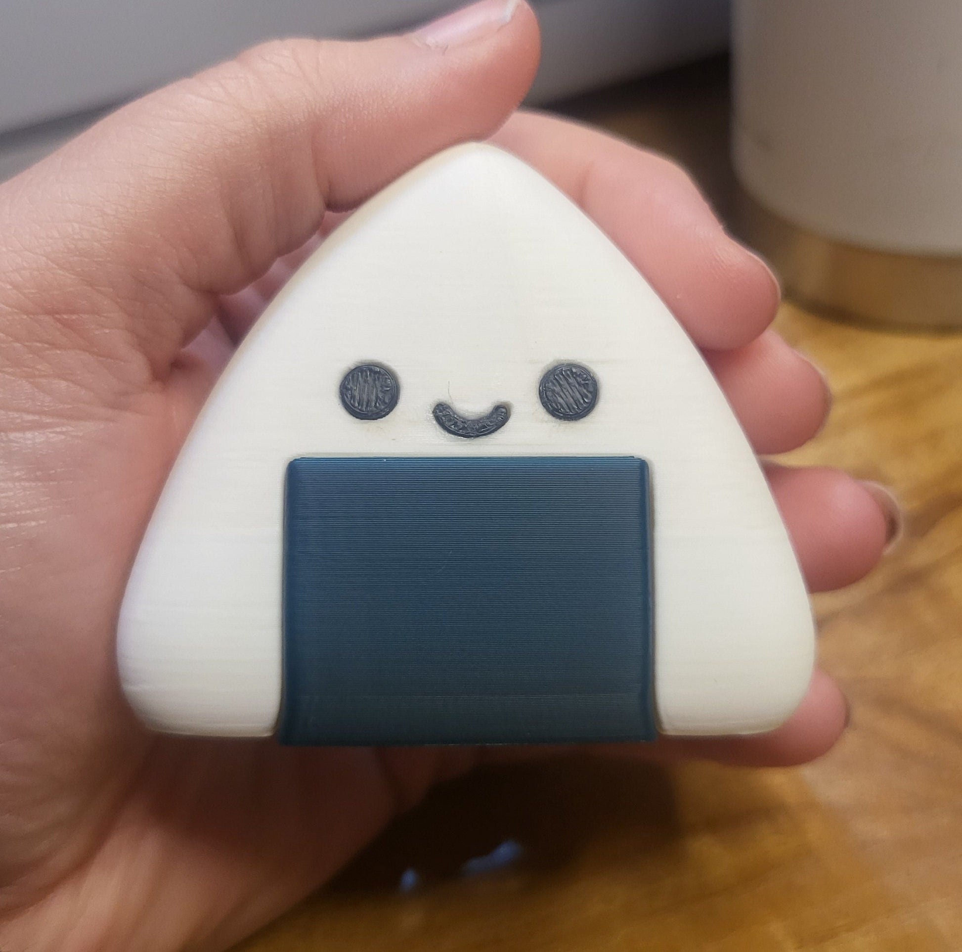 3D printed onigiri figure held in a hand for size reference — about 2 inches tall with smiling face and gray seaweed wrap