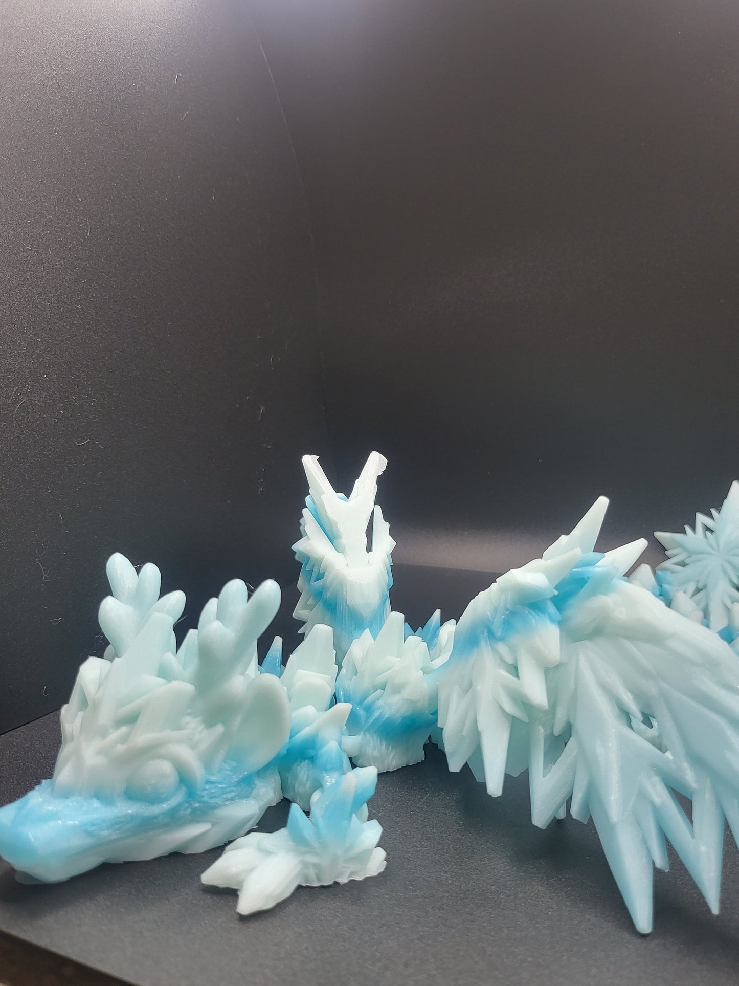 Baby Winter Dragon 3D print in side view on a dark backdrop — icy white and blue Ziro Winter gradient, crystal wings raised, snowflake accent behind