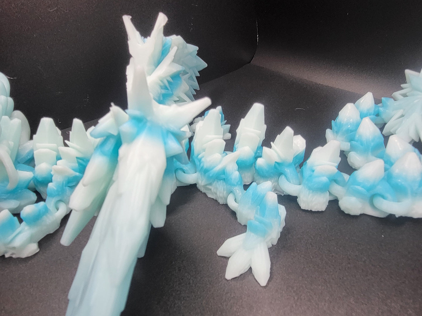 Close-up along the Baby Winter Dragon's back spines and articulated tail links — icy white and blue 3D printed segments