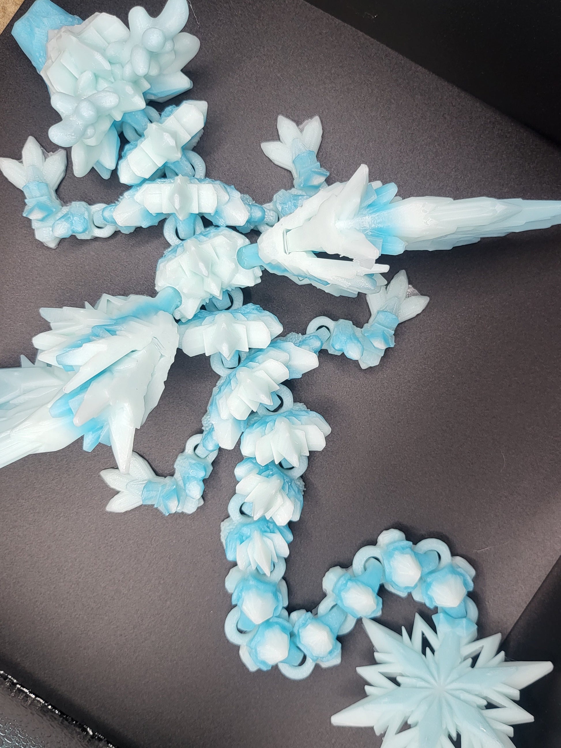 Top-down view of the Baby Winter Dragon coiled flat, showing its fully articulated segmented body and long tail — 3D printed ice-blue winter gradient