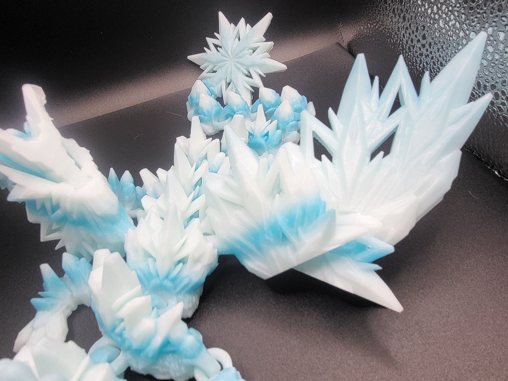 Detail of the Baby Winter Dragon's crystal-spike wings with a small snowflake perched above — 3D printed with a frost-blue gradient