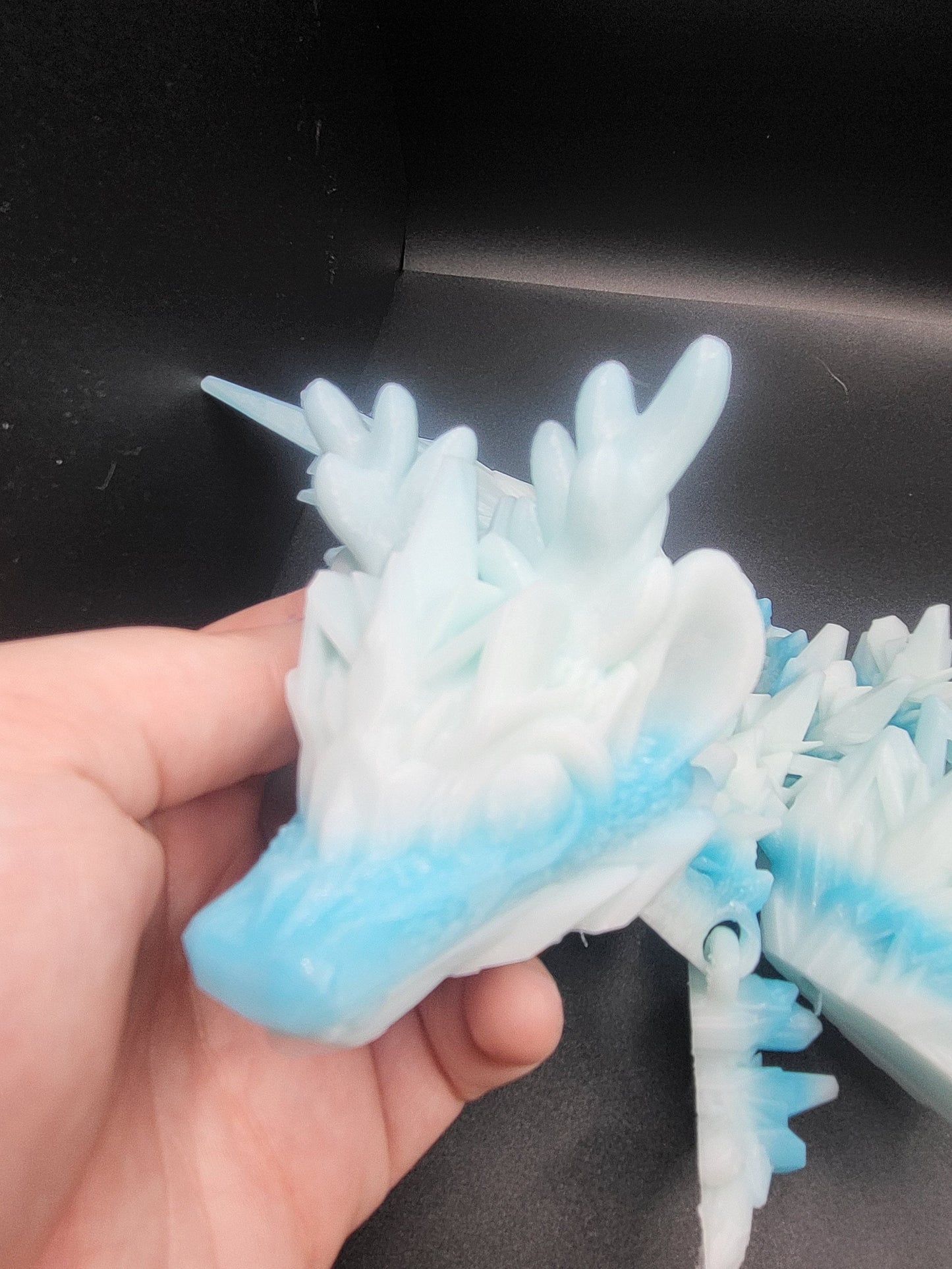 Baby Winter Dragon head held in a hand for scale — close-up of antlers, ear frills, and blue-tipped snout, 3D printed in Ziro Winter filament