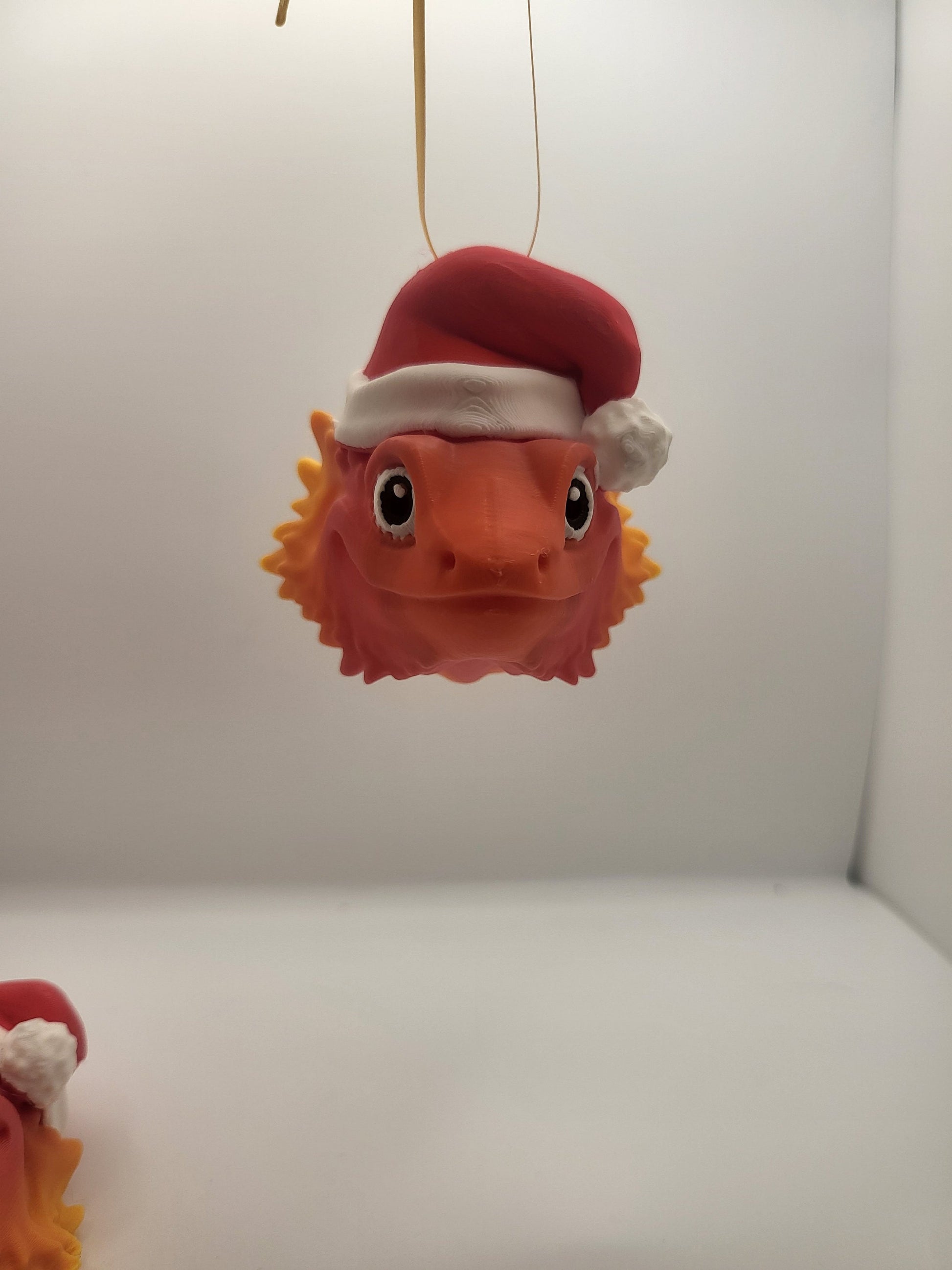 Bearded Dragon with Santa Hat Christmas ornament dangling on a ribbon with a second dragon below — 3D printed in orange gradient filament