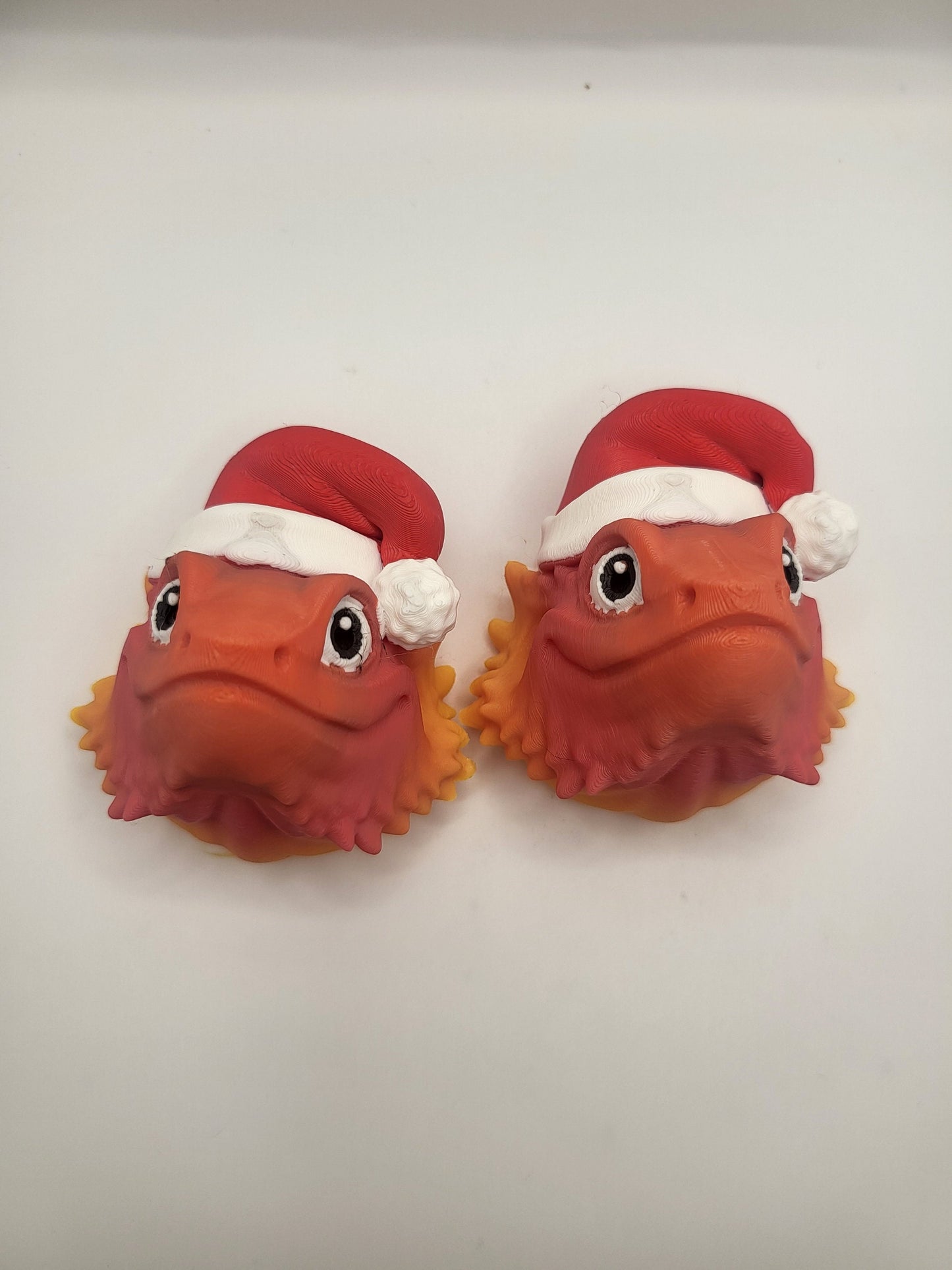 Two Bearded Dragon with Santa Hat 3D prints side by side on a white background — orange lizard faces with red Santa hats and spiky beards