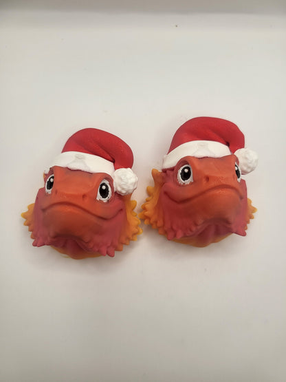 Two Bearded Dragon with Santa Hat 3D prints side by side on a white background — orange lizard faces with red Santa hats and spiky beards