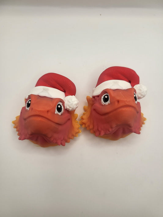 Two Bearded Dragon with Santa Hat 3D prints side by side on a white background — orange lizard faces with red Santa hats and spiky beards