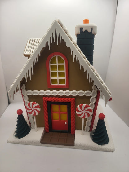 Holiday Gingerbread House Display, front view — red door with chocolate-bar step, arched window, peppermint lollipops and pine trees, 3D printed