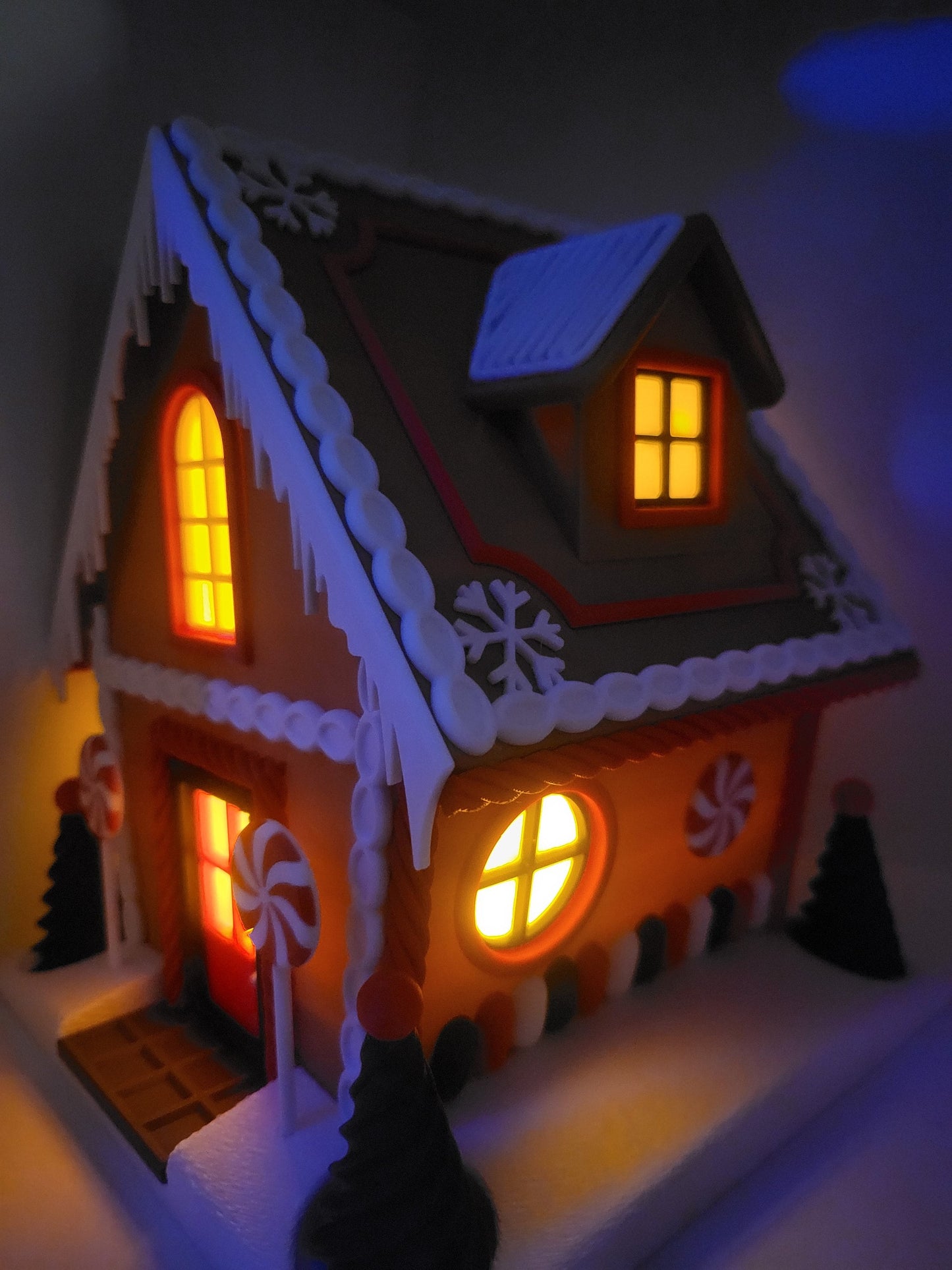 Holiday Gingerbread House Display glowing at night — 3D printed house lit from within, warm light shining through the windows and dormer