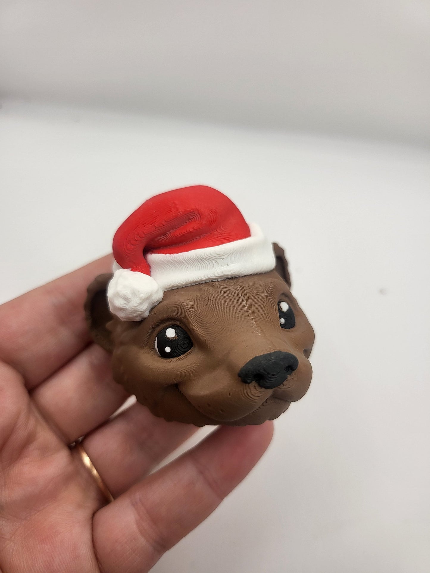 Ferret with Santa Hat ornament held in a hand — brown filament ferret face with red and white Santa hat, 3D printed