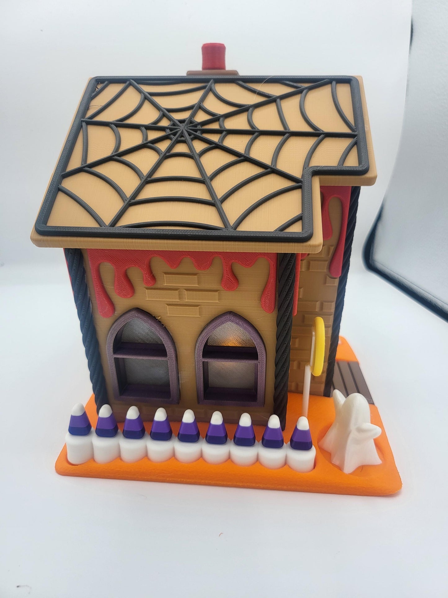 Halloween Gingerbread House side view — candy corn fence posts lining the orange base, ghost figurine, and lollipop sign beside the brick-textured wall, 3D printed