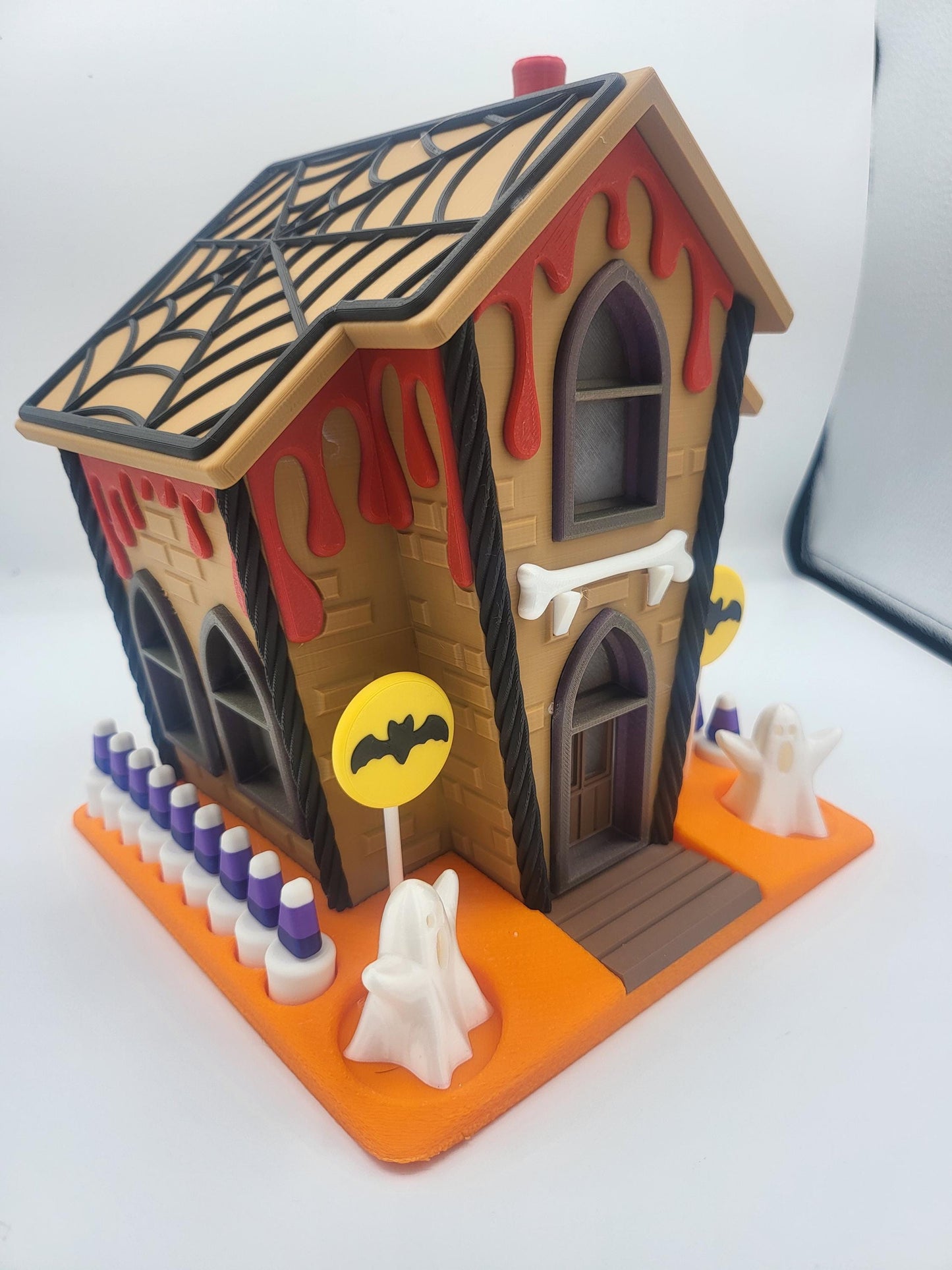Halloween Gingerbread House angled view showing the black spiderweb roof, dripping red ooze, bone sign, ghost figurines, and candy corn fence posts — 3D printed decoration