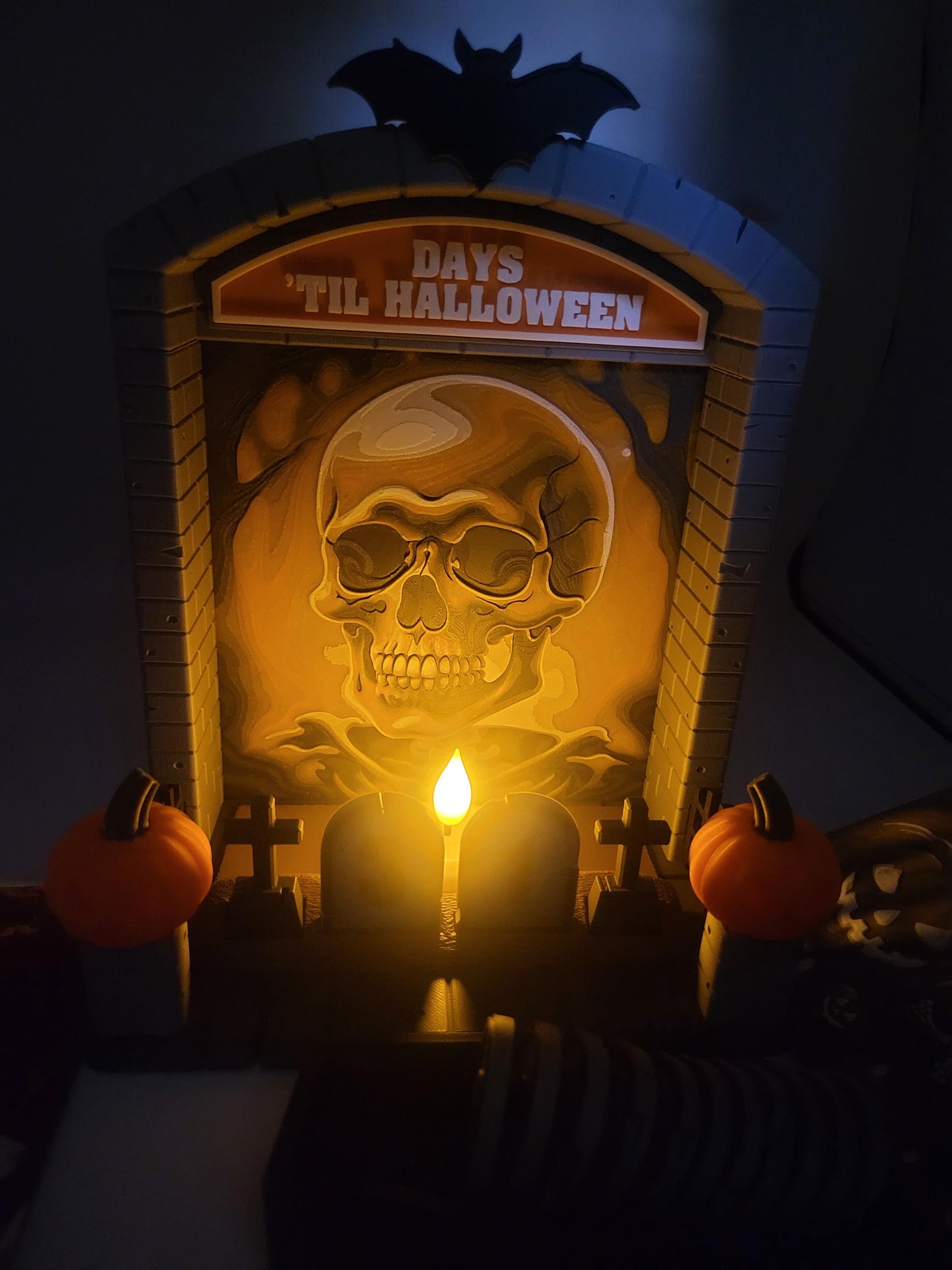 Halloween Countdown skull backdrop lit at night — flameless tealight candle casting a warm glow across the Hueforge skull scene, 3D printed