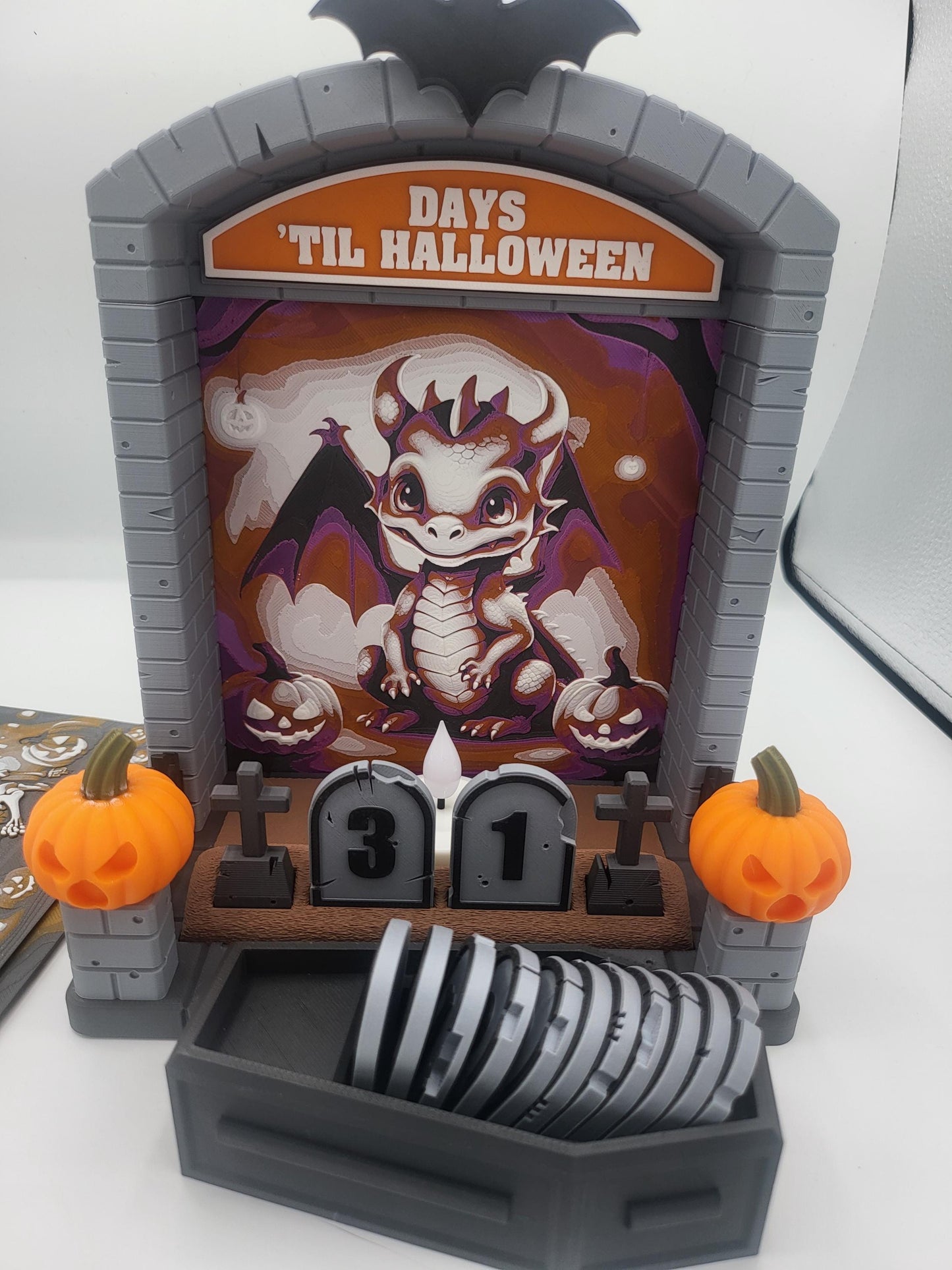 Halloween Countdown with cute dragon backdrop — 3D printed tombstone frame reading Days Til Halloween, coffin tombstone numbers set to 31, pumpkins on the pillars