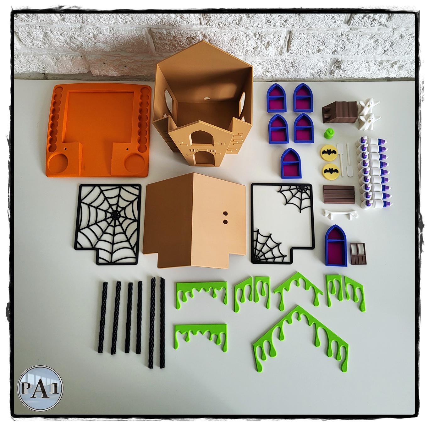 Halloween Gingerbread House DIY kit — all 3D printed parts laid out flat, shown in an alternate colorway with green ooze drips, blue windows, and spiderweb panels