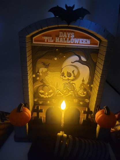 Halloween Countdown glowing in the dark — LED tealight illuminating the skeleton graveyard backdrop with warm candlelight, pumpkin pillars aglow, 3D printed