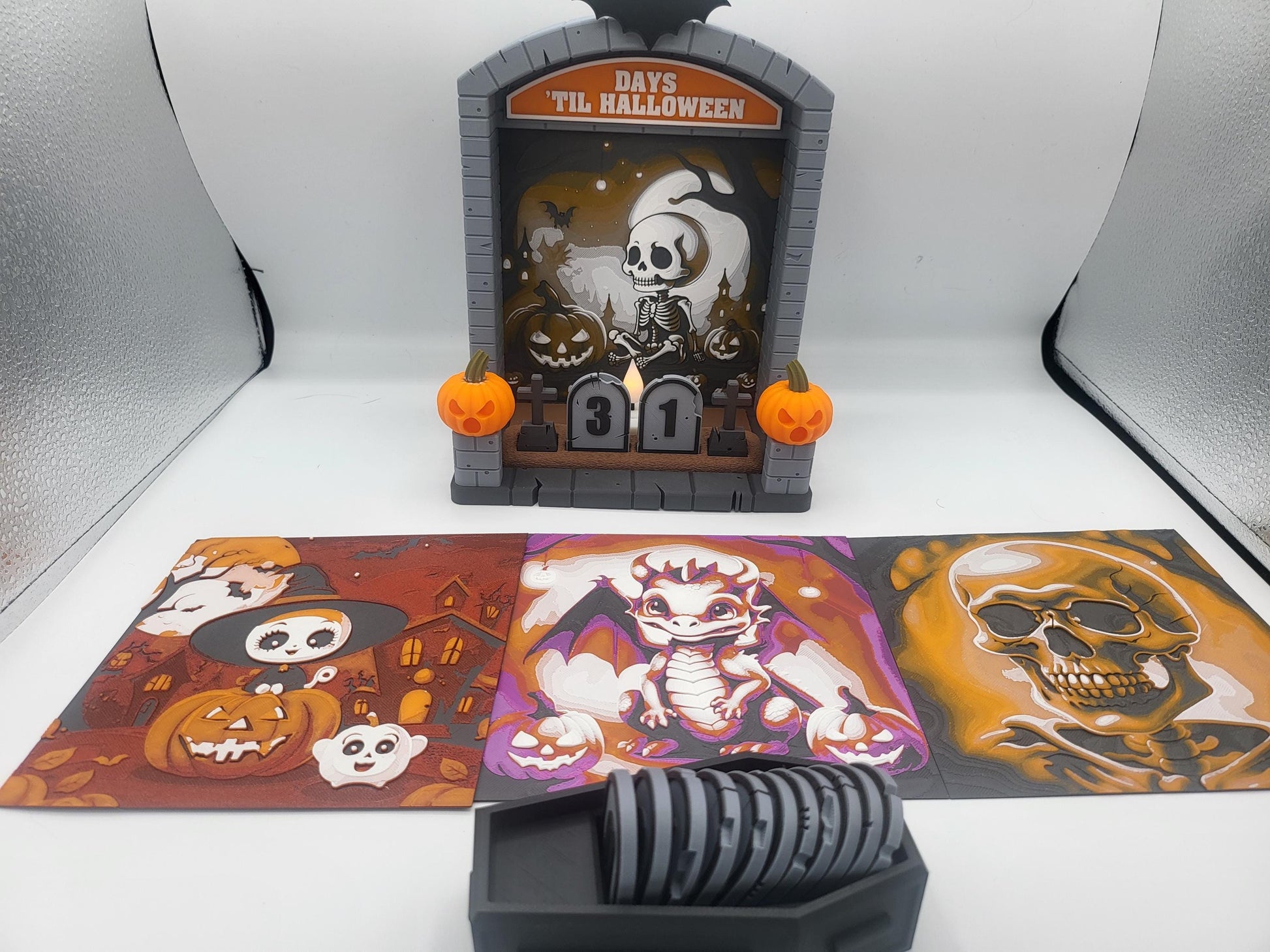 Halloween Countdown full set — skeleton backdrop installed with the pumpkin witch, dragon, and skull swap-out backdrops laid out in front, plus coffin number storage, 3D printed