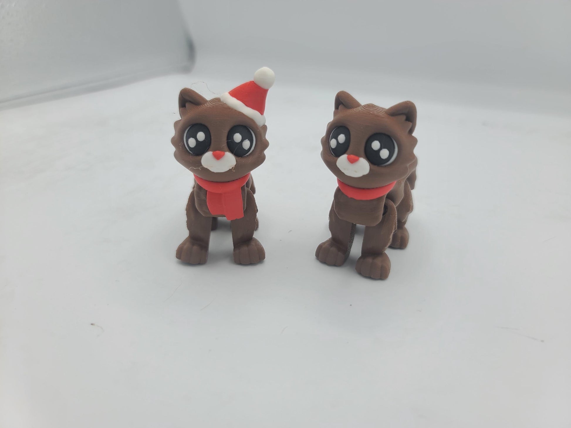 Cocoa Kitty flexi cats standing side by side facing forward — Santa Hat and No Hat styles, 3D printed in cocoa brown with big sparkly eyes