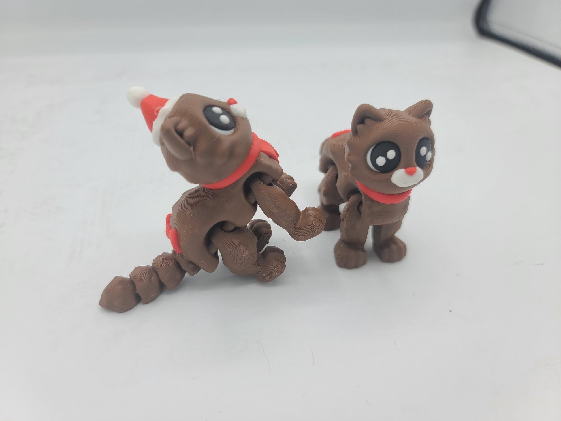 Side view of the Cocoa Kitties at play — Santa Hat kitty rearing up with segmented tail curled while the No Hat kitty stands nearby, 3D printed