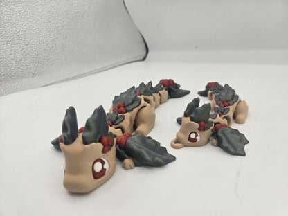 Full size and keychain sized Mistletoe Dragon flexis side by side — beige articulated 3D printed dragons with holly leaf wings and red berries
