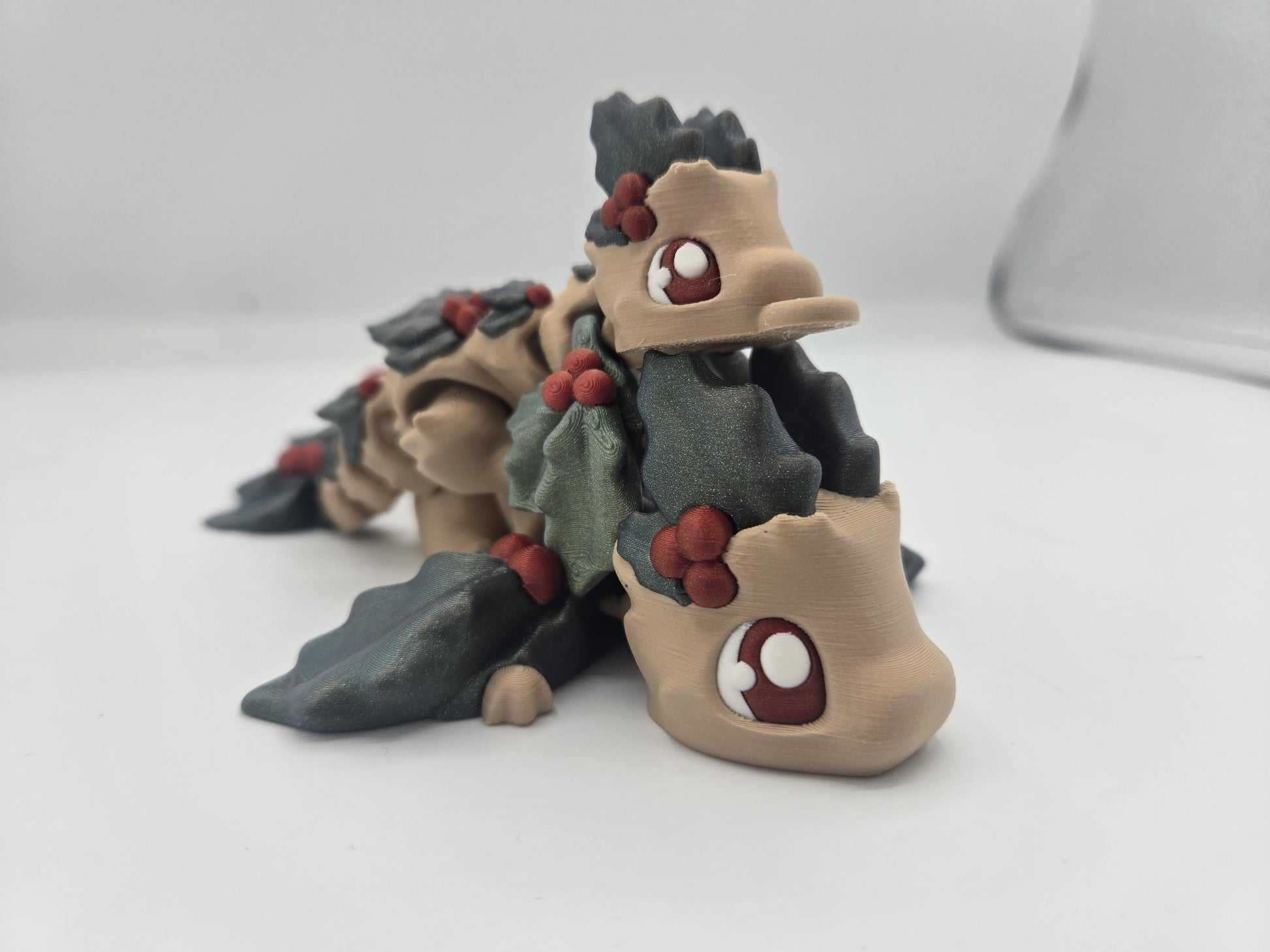 Mistletoe Dragon flexi close-up — beige 3D printed dragons with dark holly leaves, red berries, and big red-and-white cartoon eyes