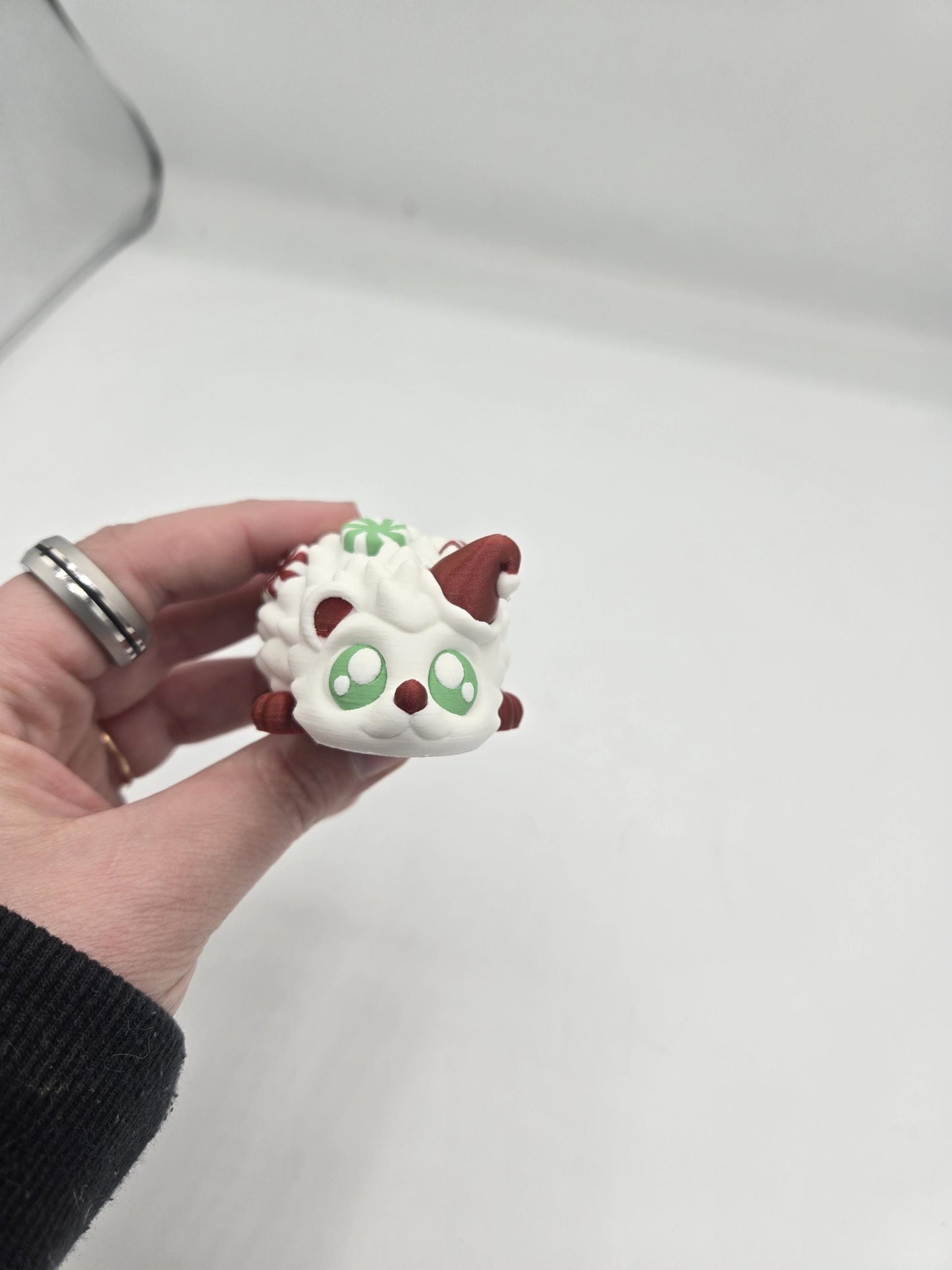 Peppermint Candies Christmas Hedgehog flexi held in hand, face view — cute green-eyed face under a red Santa hat, 3D printed