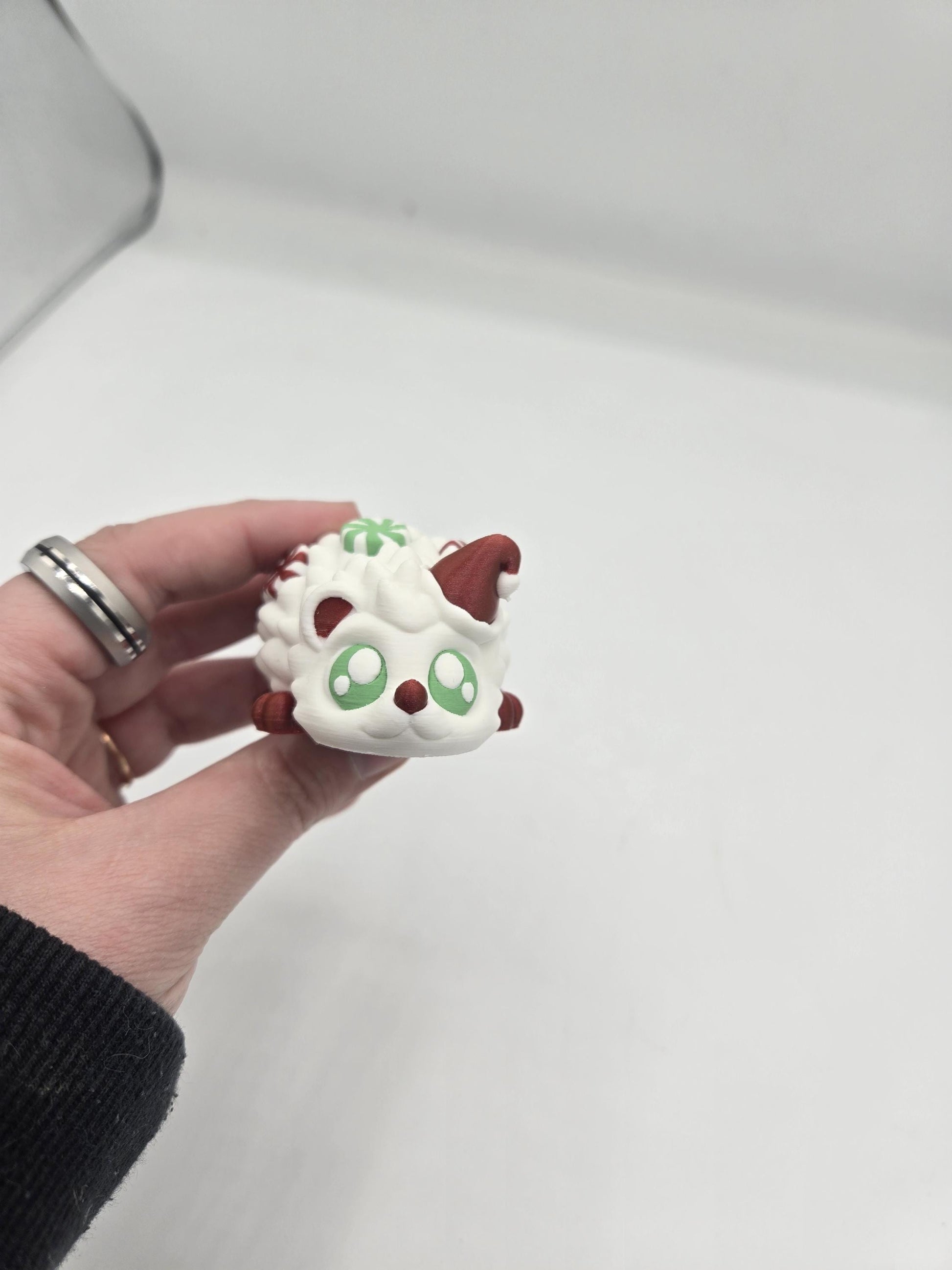 Peppermint Candies Christmas Hedgehog flexi held in hand, face view — cute green-eyed face under a red Santa hat, 3D printed