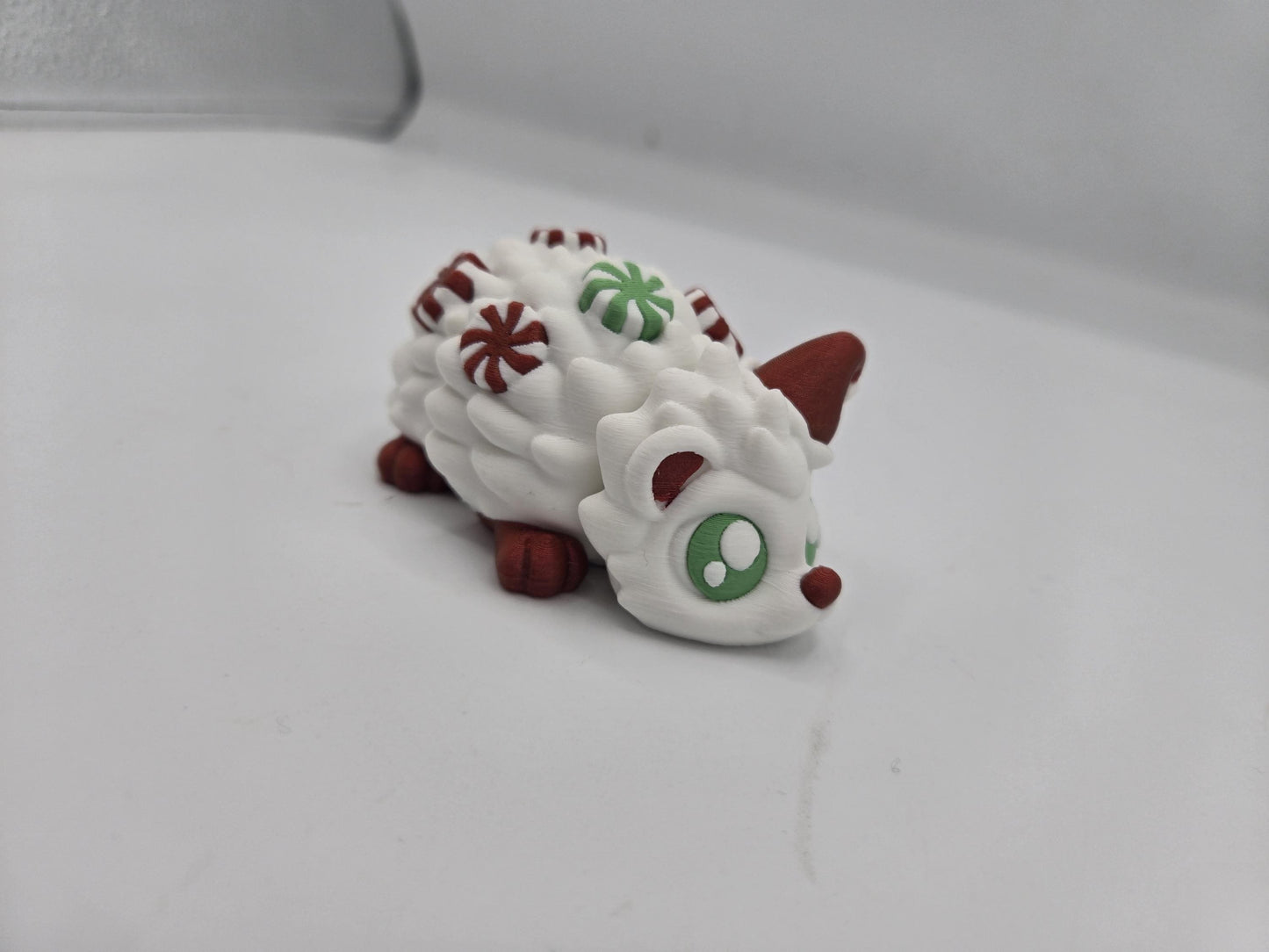 Peppermint Candies Christmas Hedgehog flexi, three-quarter front view — big green eyes, red Santa hat, and mint candy accents, 3D printed