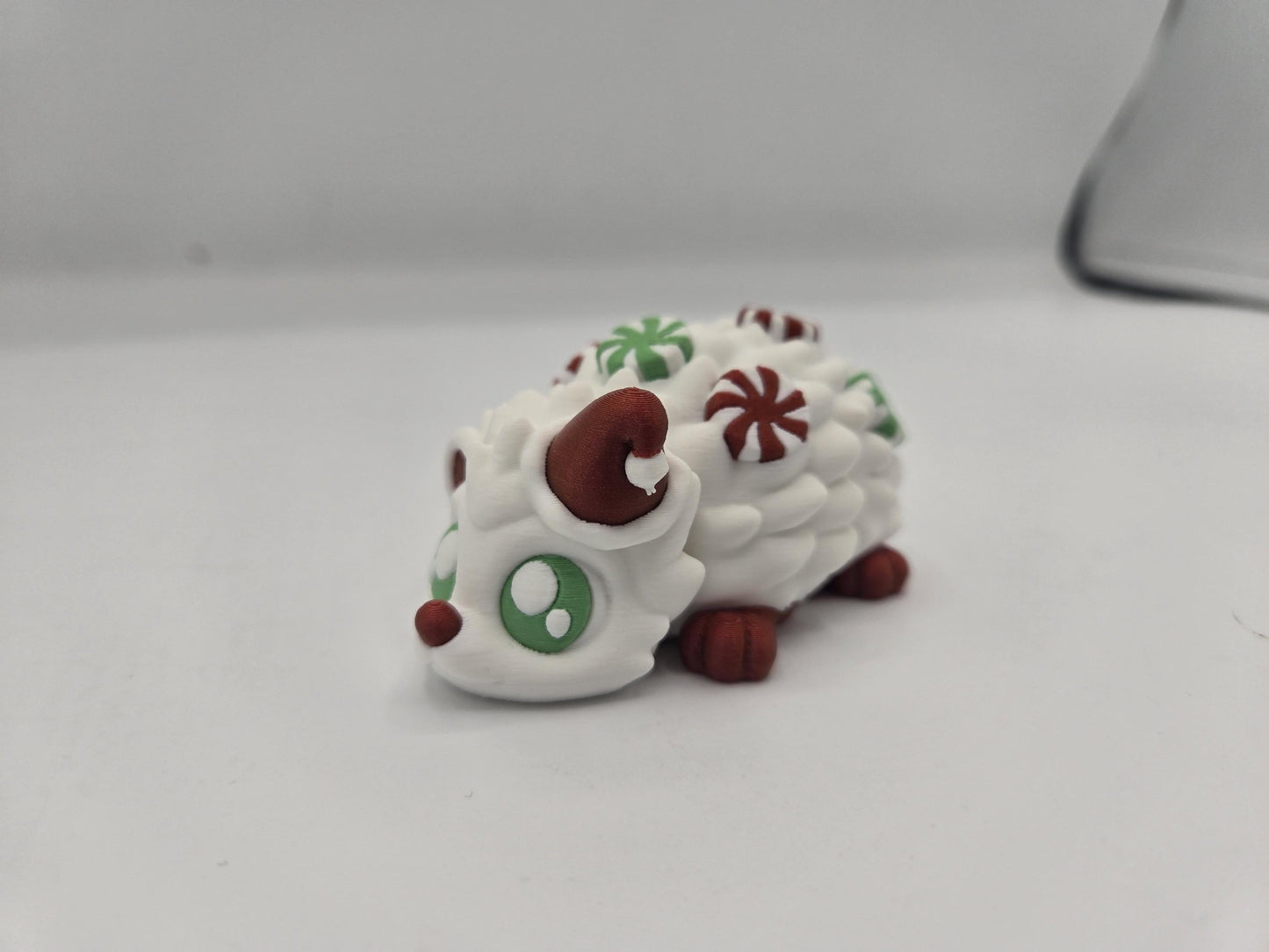 Peppermint Candies Christmas Hedgehog flexi, 3D printed — white hedgehog with Santa hat, green eyes, and red and green peppermint candies along its back