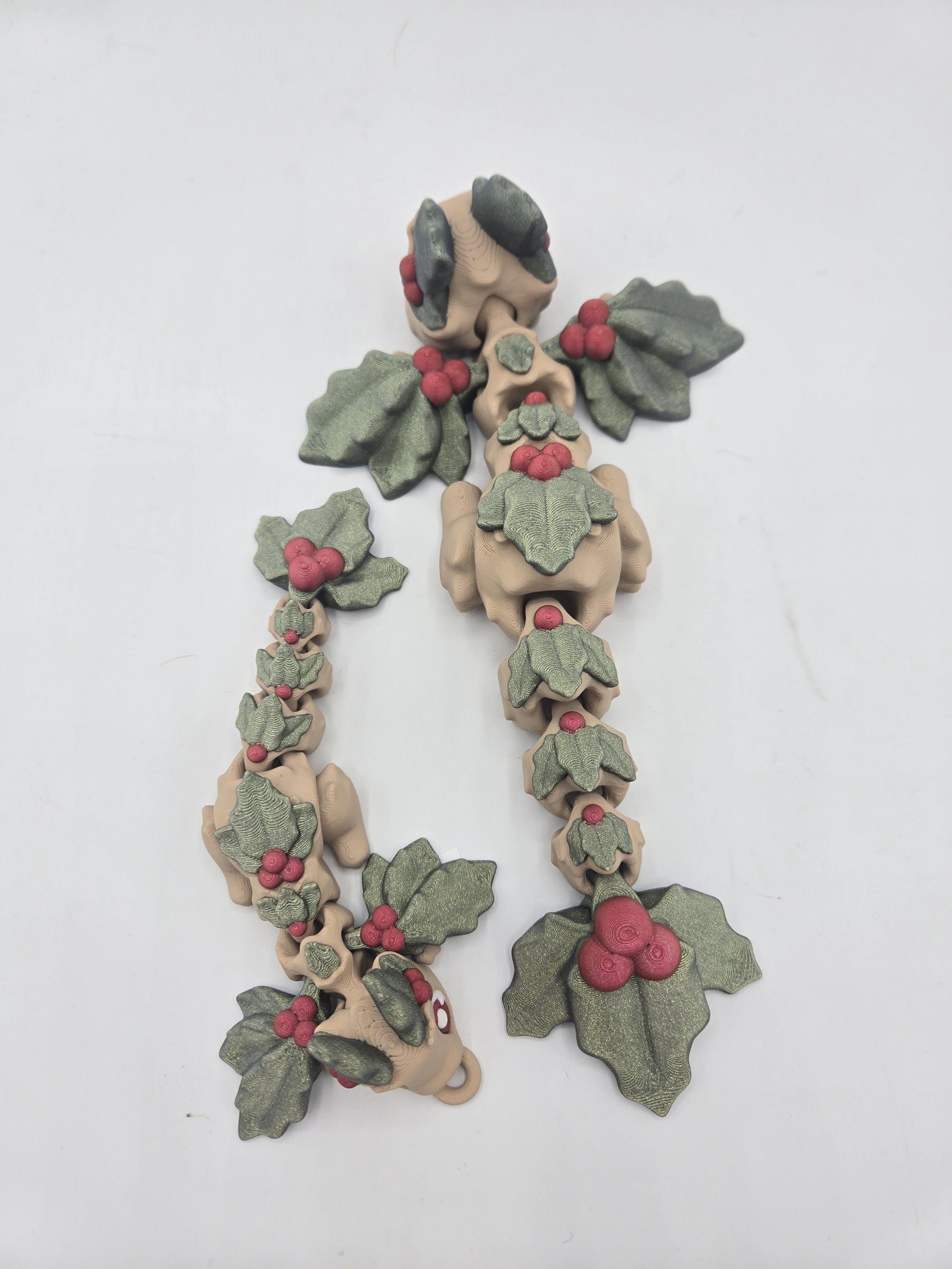 Top view of two Mistletoe Dragon flexis stretched out, showing jointed segments, holly leaf wings, and the tail keychain loop — 3D printed