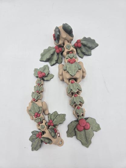 Top view of two Mistletoe Dragon flexis stretched out, showing jointed segments, holly leaf wings, and the tail keychain loop — 3D printed