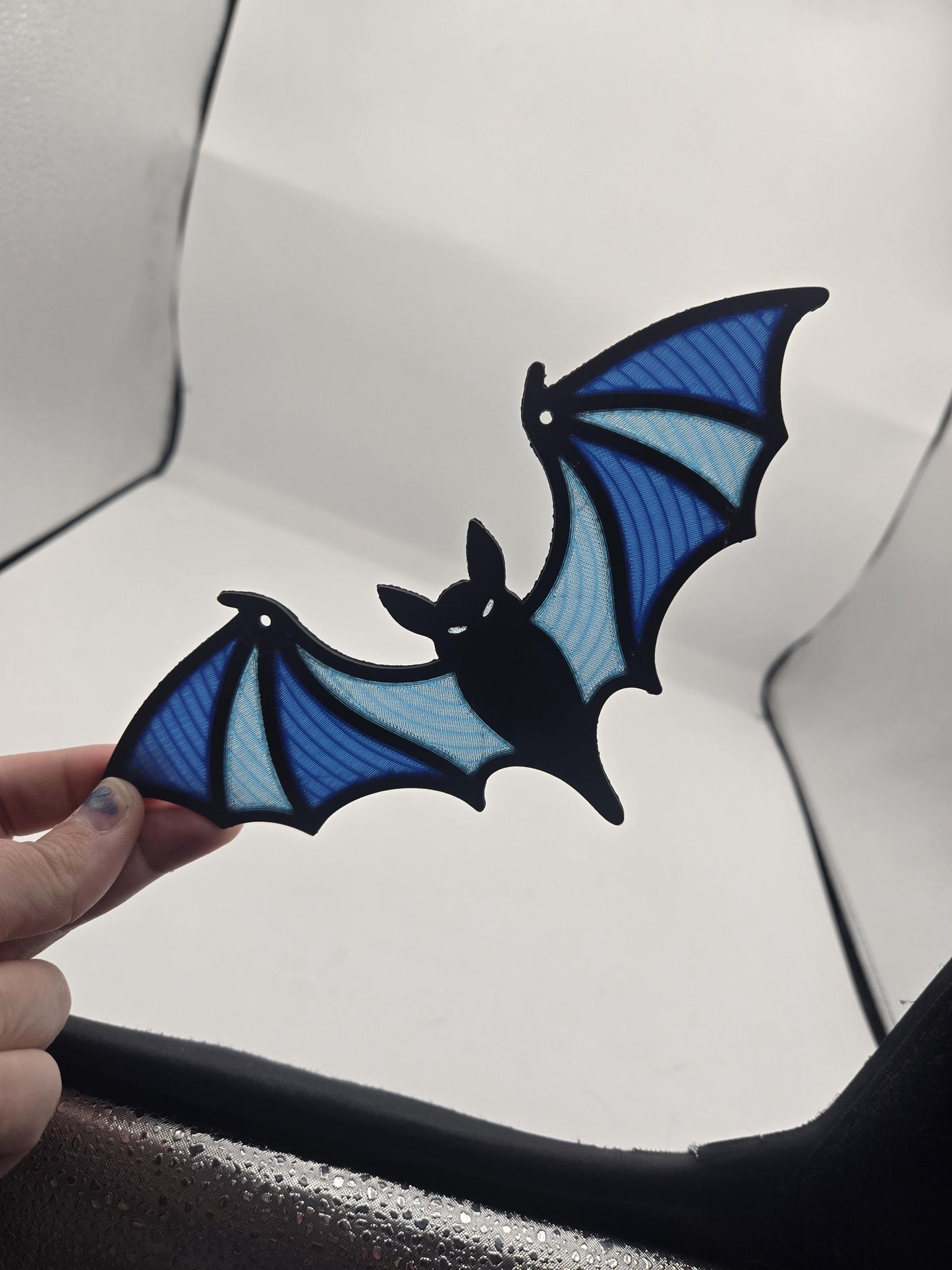 Hand holding the spooky bat stained glass style decor showing its full wingspan and blue panel gradient