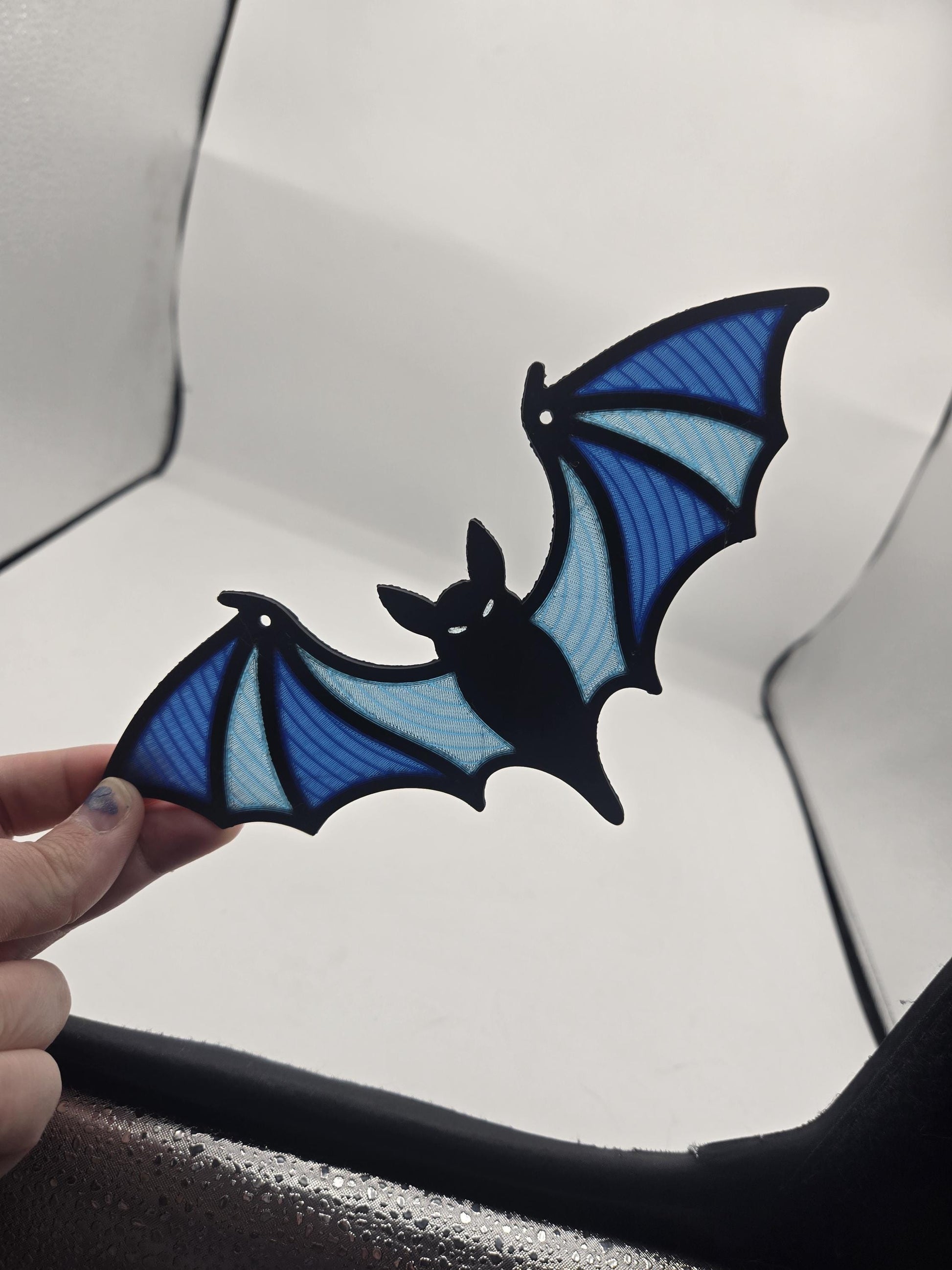 Hand holding the spooky bat stained glass style decor showing its full wingspan and blue panel gradient