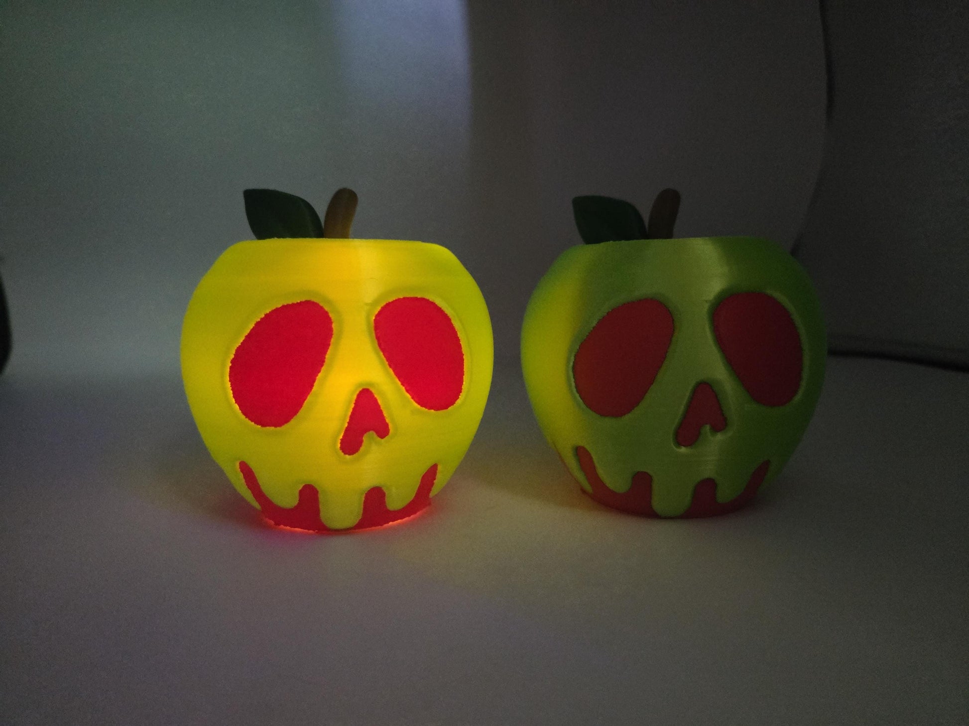 Two 3D printed poison apple displays glowing in the dark with LED tealights inside, skull faces lit up