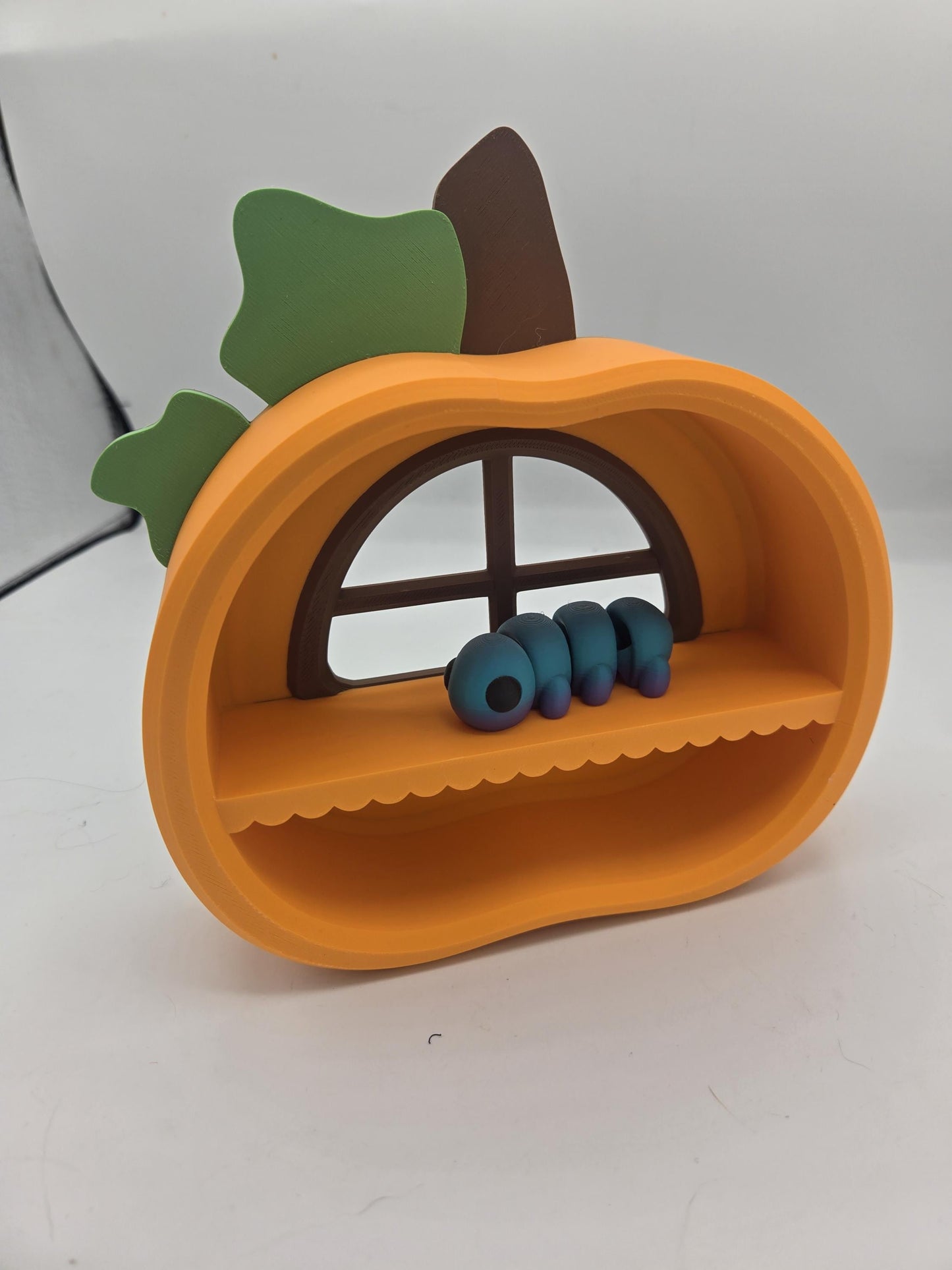 Pumpkin Trinket Shelf with a blue caterpillar flexi resting by the window — orange 3D printed pumpkin shelf for tiny treasures