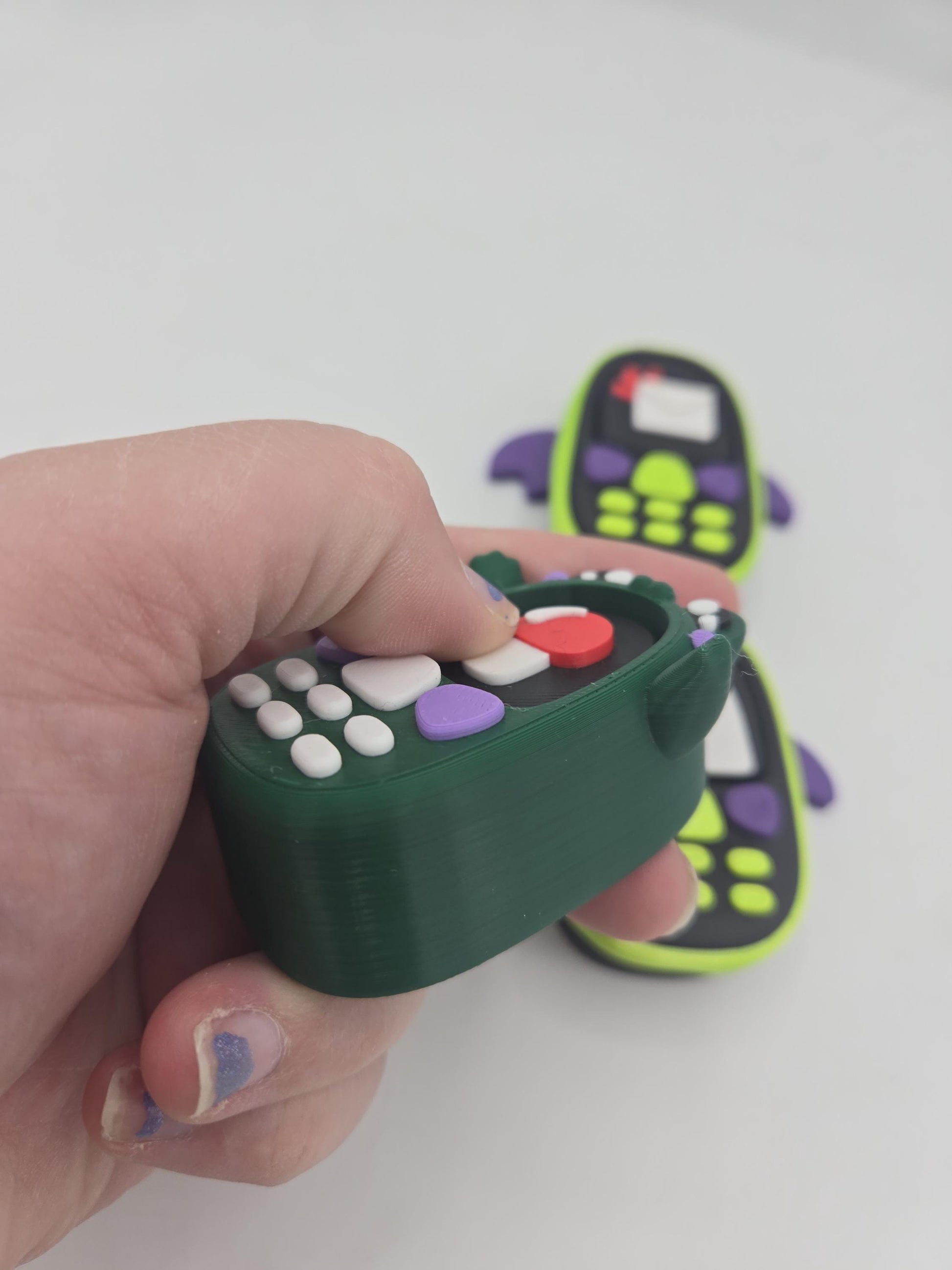 Kawaii frog phone clicker held in hand — thumb pressing the mechanical key switch screen, bat phone clickers in the background, 3D printed
