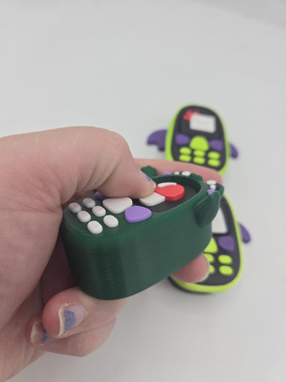 Kawaii frog phone clicker held in hand — thumb pressing the mechanical key switch screen, bat phone clickers in the background, 3D printed