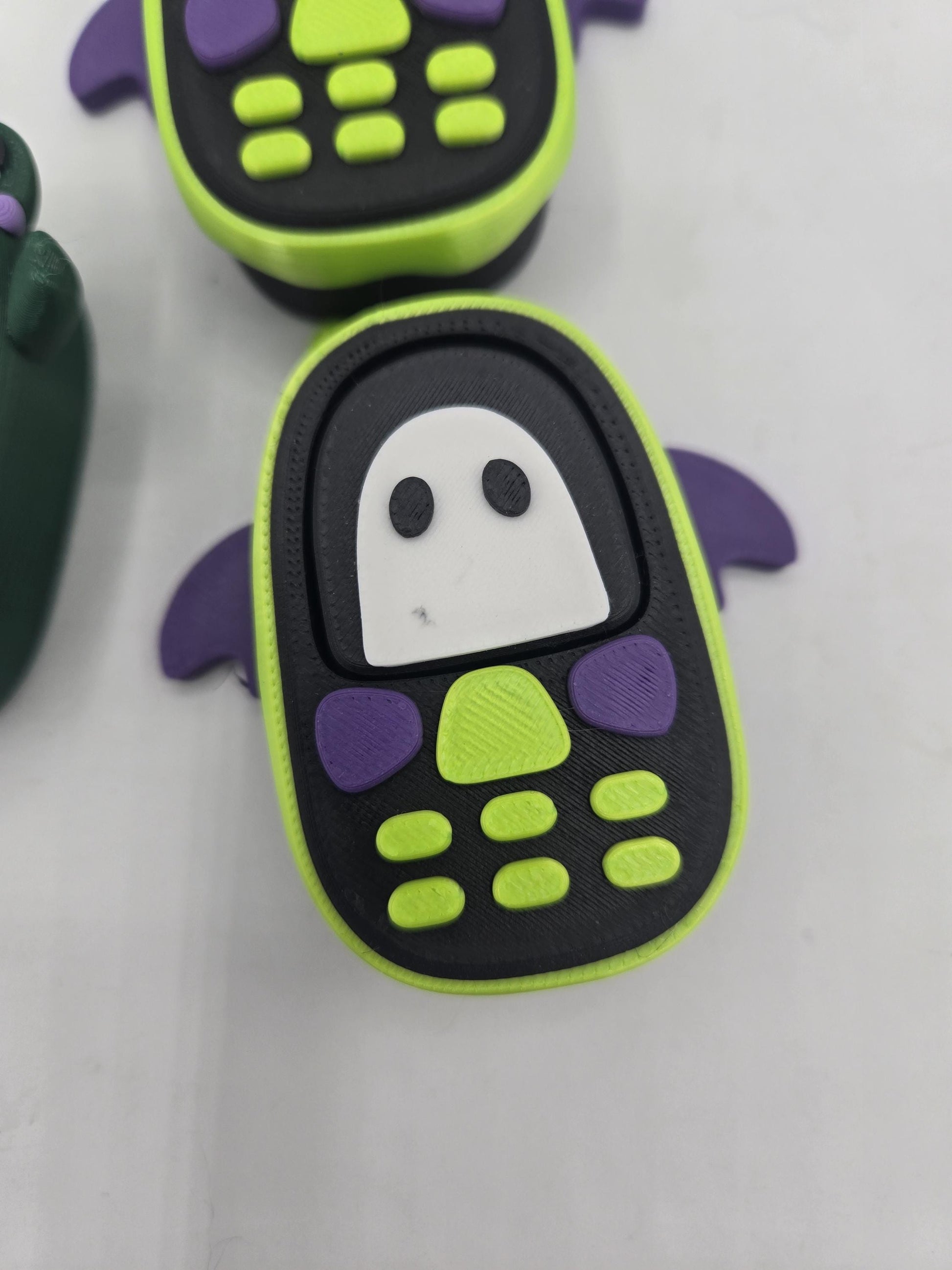 Kawaii bat phone clicker close-up — lime green phone with purple bat wings and white ghost screen design, 3D printed