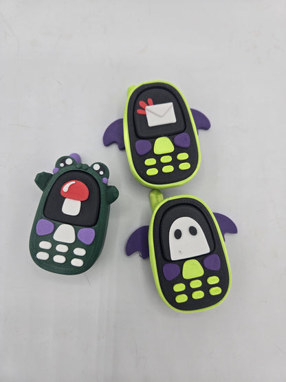Kawaii phone mechanical key clickers, 3D printed — green frog phone with mushroom screen beside lime bat phones with envelope and ghost screens