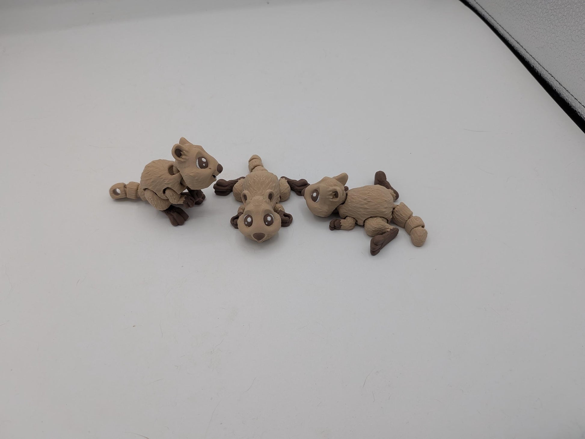 Three poseable mini quokka 3D prints showing flexible bodies and keychain hole options from multiple angles