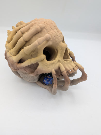 Angled view of the skull dice tower with skeletal hands gripping the crown and a blue d20 in the catch tray