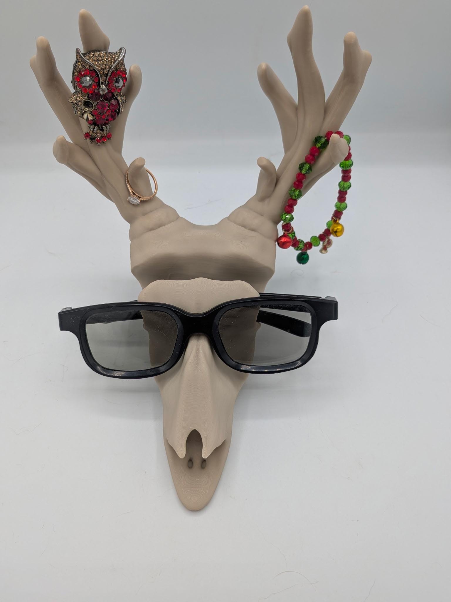 Deer skull stand wearing glasses across the brow with a ring, brooch, and beaded bracelet hung on the antlers