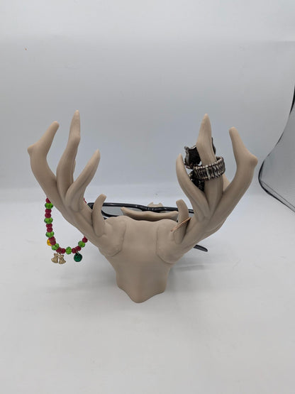 Back view of the deer skull stand holding glasses, rings, and a beaded bracelet on its antlers