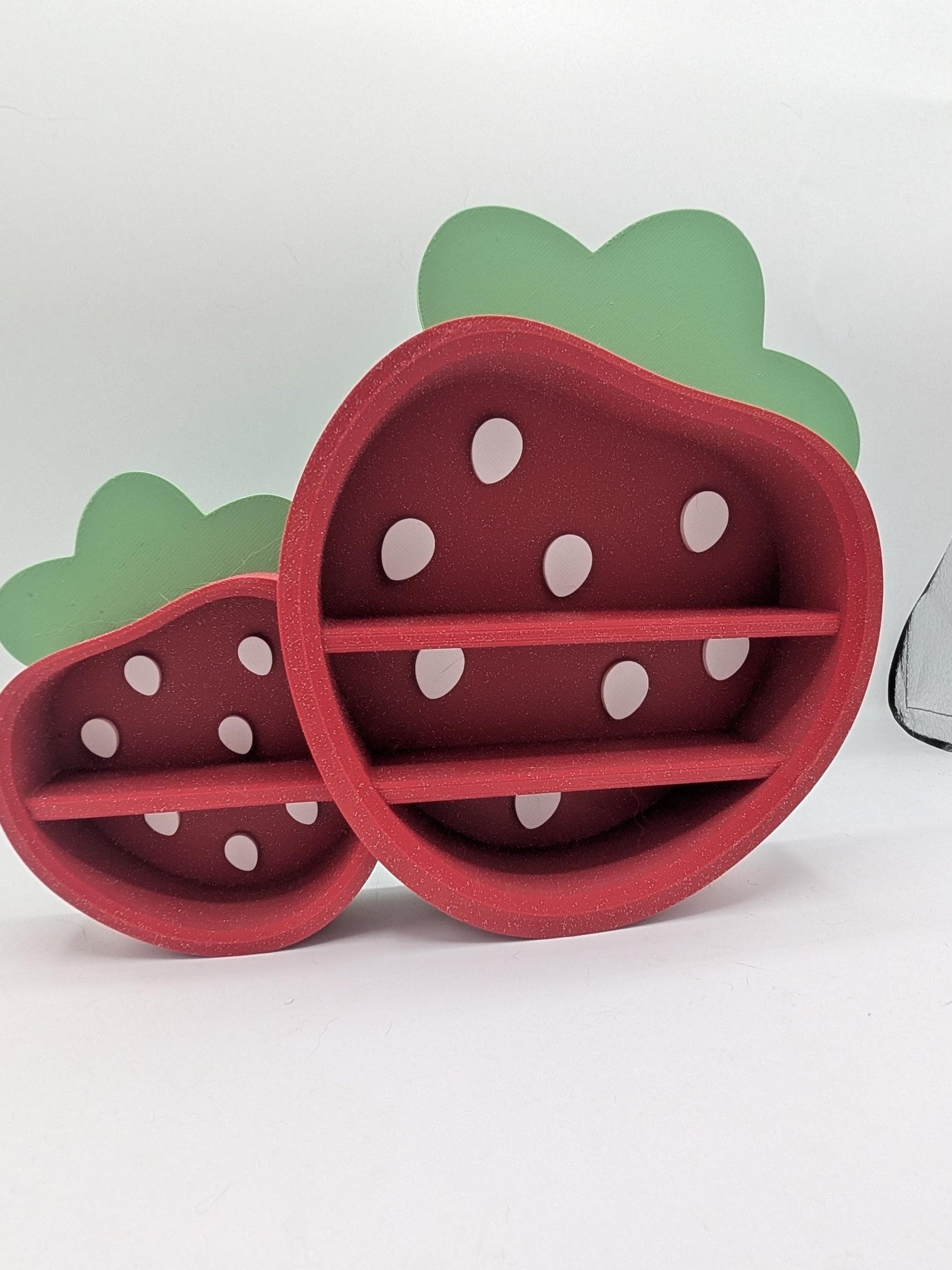 Strawberry Trinket Shelf angled view — 3D printed red strawberry display shelves with white seed details and green leaf tops, large and small sizes